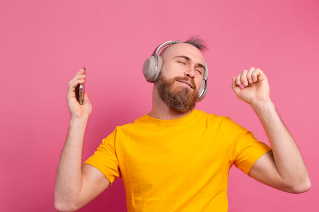 耳机帅哥带着手机和耳机在粉色背景上翩翩起舞使用音频头发