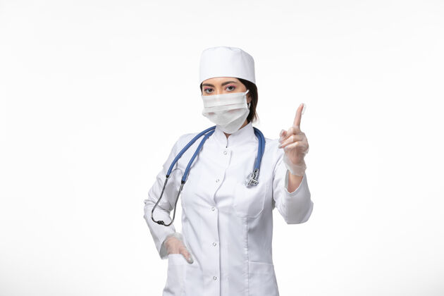 冠状病毒防护正面图：女医生穿着白色无菌医疗服 戴着口罩 因为柯维德在白墙上冒充疾病柯维德大流行疾病姿势人员药品