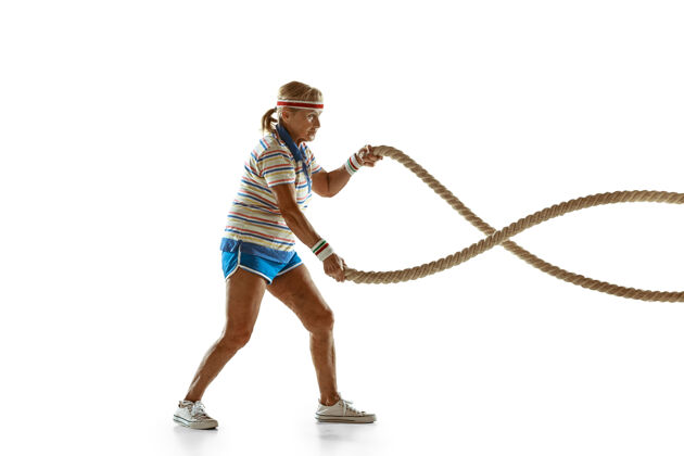 爱好穿运动服在白墙上用绳子训练的高级女子乐趣玩快乐