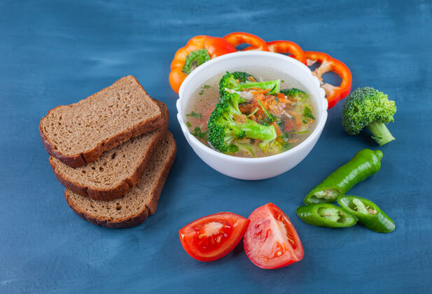 汤一碗鸡汤 蔬菜和面包放在蓝色的表面上美味碗蛋白质