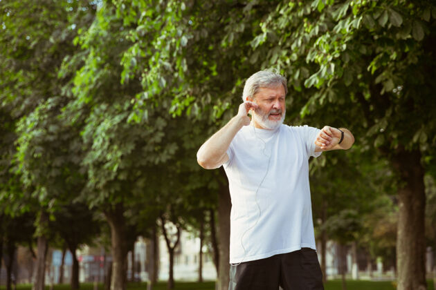 头发高级男子作为跑步者与健身追踪器在城市的街道跑步老年人自然