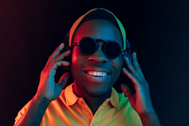 非洲年轻帅气快乐的潮人戴着耳机在黑色霓虹灯下听音乐迪斯科周末派对