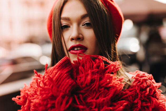 美丽一位身穿红色羊毛外套 头戴贝雷帽 皮肤黝黑 头发黝黑的妇女在城市街道的背景下看着摄像机红唇衣服直发