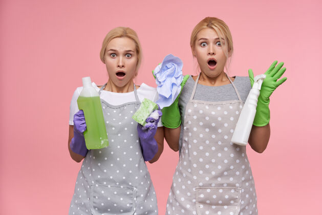 女性年轻的金发可爱的主妇们戴着橡胶手套准备春季大扫除站衣服双胞胎
