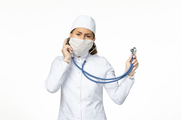 女性正面图：年轻女医生戴着无菌口罩 因为冠状病毒在白色办公桌上使用听诊器办公桌药品医疗