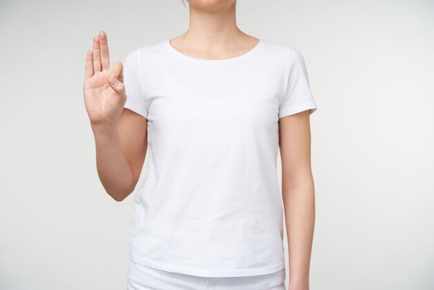 休闲摄影棚的一张照片 一位穿着休闲服的年轻女士举起手 在白色背景下展示了字母f和聋哑字母非语言符号身体