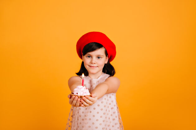 黑发可爱的孩子戴着时尚的贝雷帽庆祝生日高加索女孩儿拿着蛋糕 黄色的墙上孤立着蜡烛欢乐乐趣积极的情绪