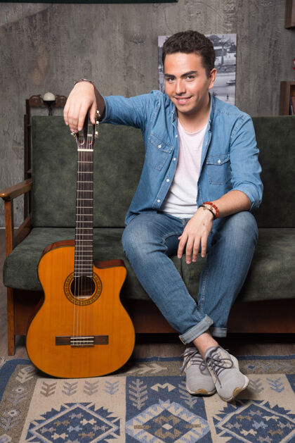 和弦微笑的吉他手拿着一把漂亮的吉他坐在沙发上高品质的照片人乐器男性