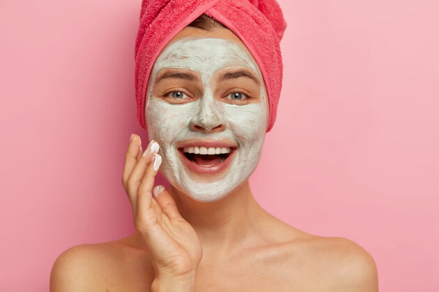 年轻贴近快乐的女性模特画像 用化妆面罩涂抹在她的脸上 有美容法 头上裹着毛巾 焕然一新 更新和治疗柔软微笑姿势
