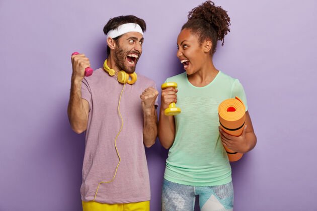 美国坚强健康情绪多变的男女欢呼雀跃 面面相觑 拿着运动器材站着 用小哑铃训练肌肉 拿着健身垫 在健身房锻炼白种人人紫色