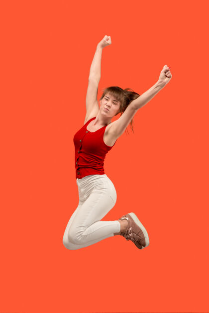 无忧无虑移动中的自由在橙色工作室背景下 美丽快乐的年轻女子跳跃和做手势的半空中镜头在运动中奔跑的女孩人类情感和面部表情的概念衣服生活方式运动