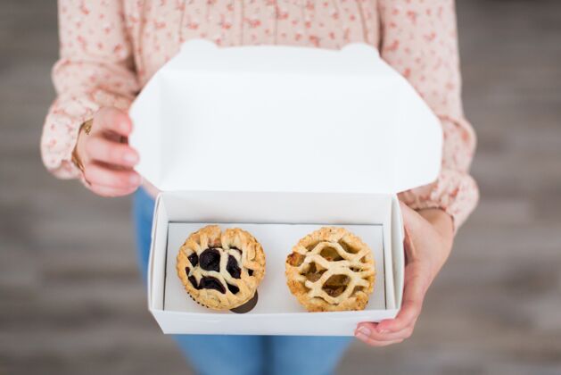 美味头顶上的一张照片 一个女人拿着一个白色的盒子 里面装着两个小糕点鲜花面包师饼干