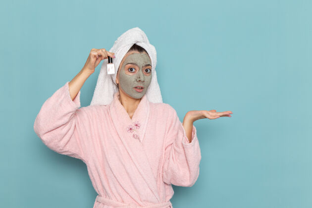 浴袍正面图年轻女性穿着粉色浴袍淋浴后拿着指甲油在蓝色墙壁上美丽的清水自护霜淋浴抛光奶油人