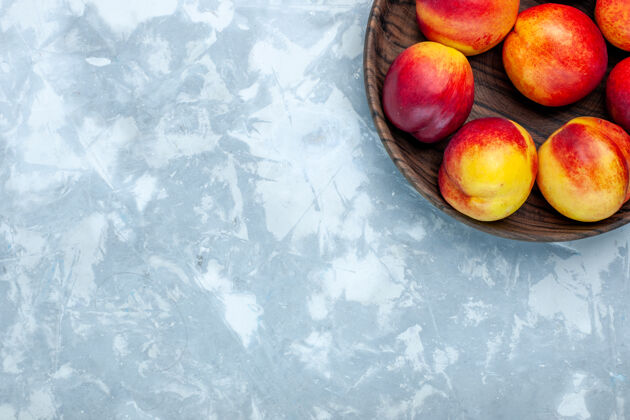 可食用水果顶视图新鲜桃子醇厚可口的水果内棕色盘子在浅白色的办公桌上健康油桃新鲜