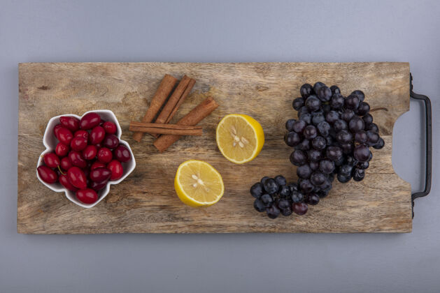 新鲜顶视图新鲜的红色山茱萸浆果与柠檬肉桂棒和葡萄在木制厨房板上的灰色背景山茱萸肉桂木头