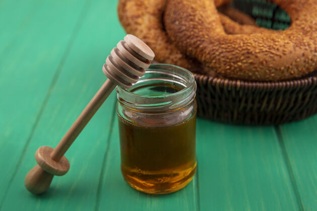 玻璃玻璃罐上蜂蜜的俯视图 木制蜂蜜勺和绿色木制背景上的一桶面包罐子天然木头
