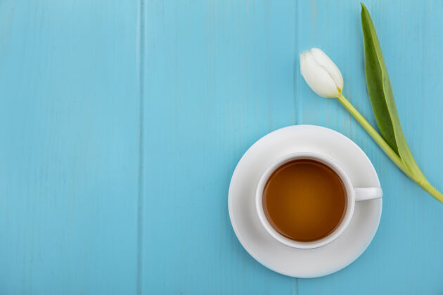 视图一杯茶的俯视图 蓝色木质背景上有美丽的白色郁金香 还有复印空间蓝色茶桌子