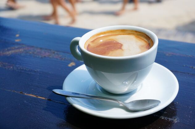 咖啡馆特写镜头：一杯咖啡放在一个带金属勺子的白色碟子上早餐桌子马克杯