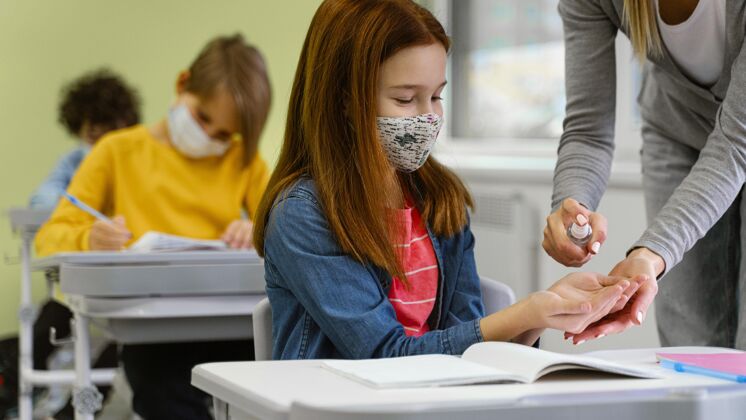 流行病戴着医用口罩的学生从老师那里得到洗手液返校学习教育