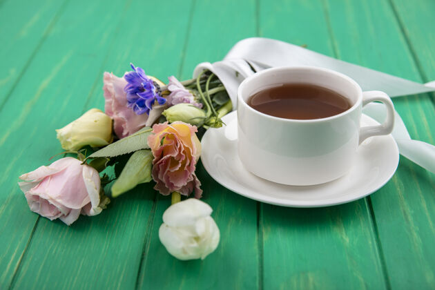 杯子茶碟上的茶杯和绿色背景上的花束的侧视图茶碟绿色桌子