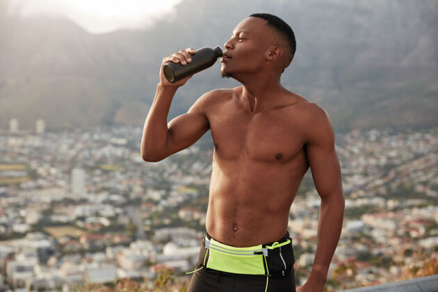 户外身体运动的黑人男子的水平镜头 用水补充水分 拿着瓶子 有氧运动后感觉口渴 中风呼吸 感觉脱水 与山景对抗慢跑跑步非洲