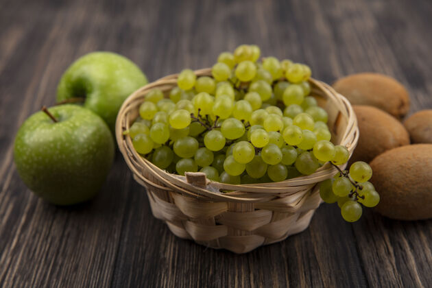 植物正面图绿色的葡萄在一个篮子里 绿色的苹果和猕猴桃在木制的背景上猕猴桃水果葡萄