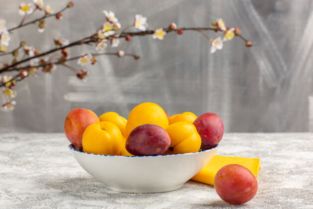 食品正面图新鲜甜杏黄色水果盘内与李子在白色表面可食用水果水果健康