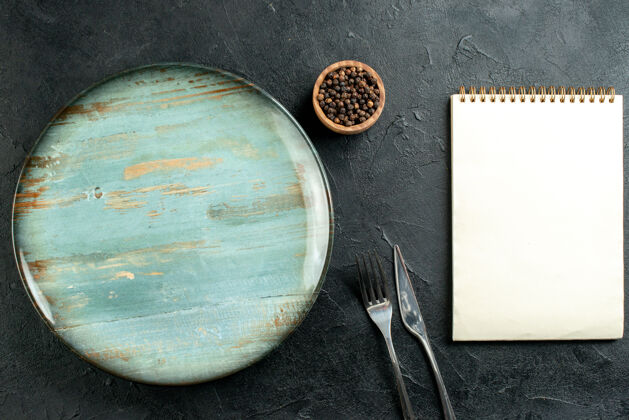 晚餐顶视图圆形盘子餐刀和叉子黑胡椒在碗记事本在黑桌子上叉子圆盘子顶部