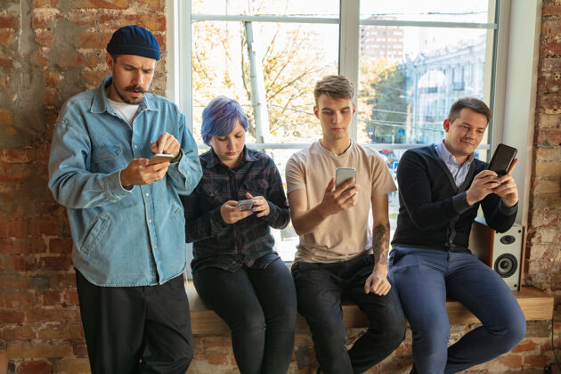 房子一群快乐的白人年轻人站在窗户后面分享新闻 照片或智能手机上的视频 聊天或玩游戏 享受乐趣社交媒体 现代科技平板电脑女性观看