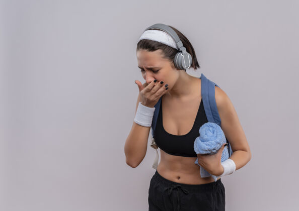 运动穿着运动服 背着背包 头上戴着耳机 拿着毛巾 站在白墙上咳嗽 看起来很不舒服年轻人女性人