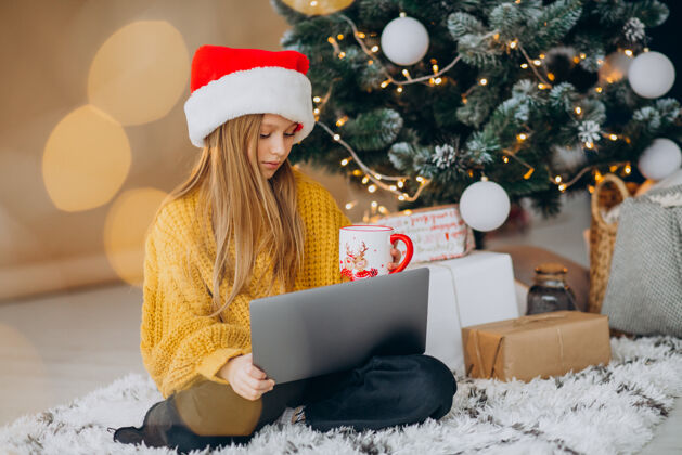 笔记本电脑可爱的女孩在圣诞树旁用电脑圣诞圣诞树庆祝