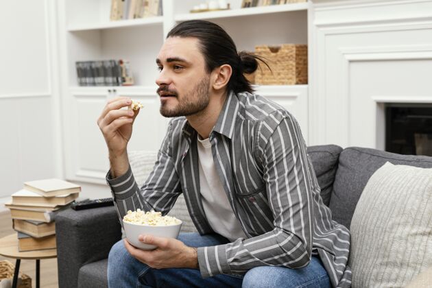 家男人在沙发上吃爆米花看电视男性室内无忧无虑