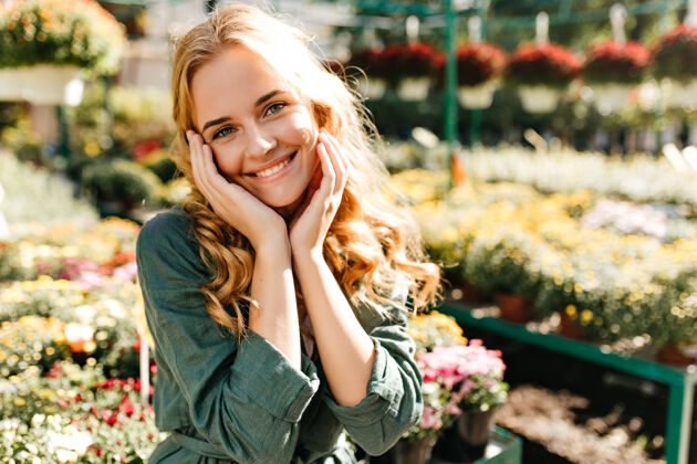 花一位金发碧眼 笑容温柔的年轻女子 身着绿色长袍 系着腰带 正在温室里工作公园肖像花束
