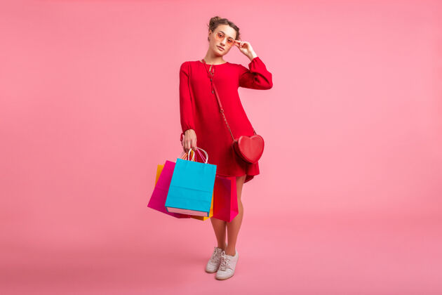 女性迷人快乐微笑的时尚女性购物狂身着红色新潮连衣裙手持五颜六色的购物袋贴在粉色的墙上 销售兴奋 春夏时尚潮流长度休闲包