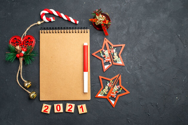 顶部顶视图红色记号笔放在笔记本上 站在一圈不同的圣诞饰品上 在黑暗孤立的自由空间表面笔记本书夹站立