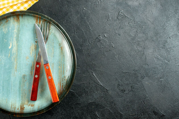 顶部上半视图刀和叉子上板黄色和白色方格餐巾在黑暗的地面上与自由空间格子盘子餐巾