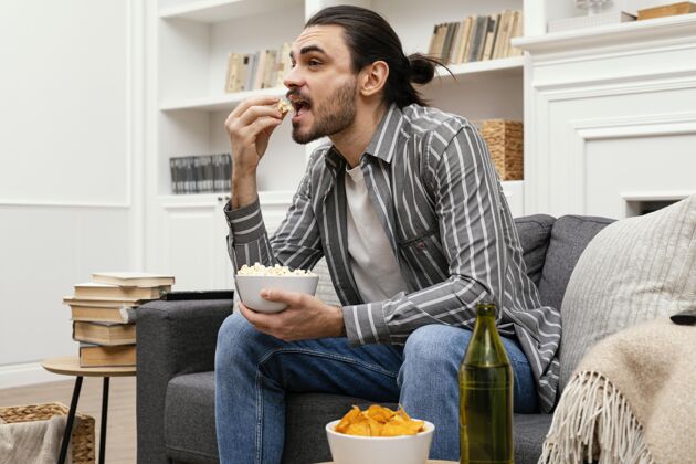 生活方式男人在沙发上吃爆米花看电视科技男性休闲时间