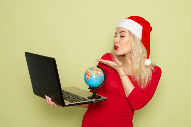 颜色正面图美丽的女性手持小地球仪 在绿色墙上使用笔记本电脑节日情感圣诞新年色彩情感歌手漂亮的女性