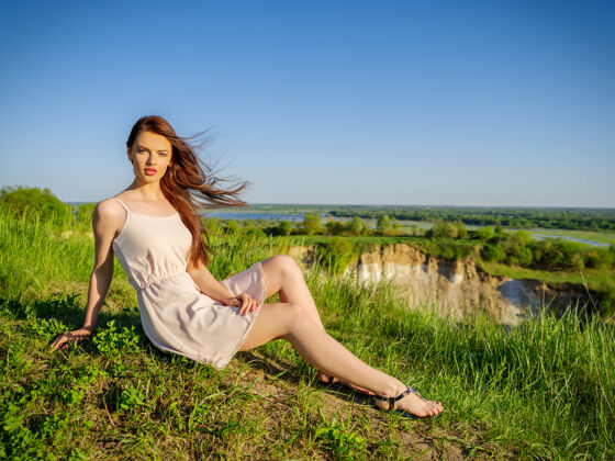 春天坐在悬崖边的年轻女子穿着白色连衣裙的漂亮女孩在户外摆姿势女模特在田野里摆姿势一个阳光明媚的夏日腿山夏天