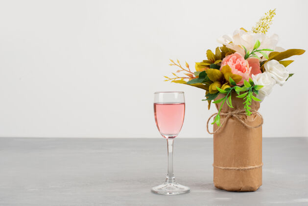 叶白色和粉色的玫瑰花束和一杯玫瑰红酒摆在灰色的桌子上开花花玻璃