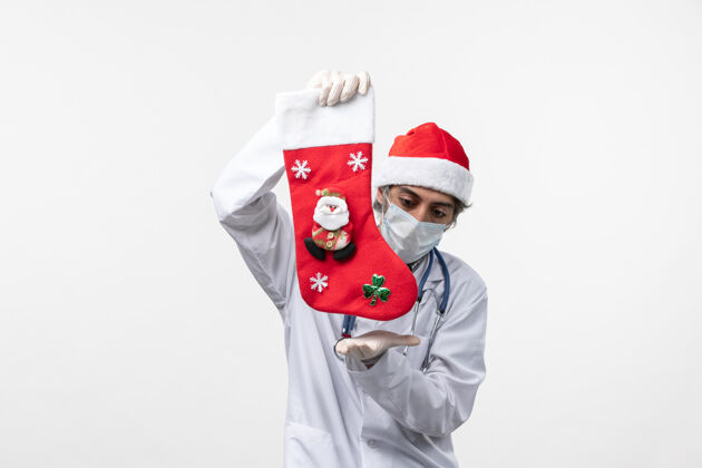 男人正面图：男医生拿着红袜子站在白墙上-圣诞病毒健康医学成人袜子