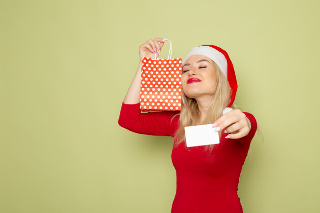 漂亮的女人正面风景美丽的女性拿着小包装礼物和银行卡在绿色的墙上情感节日圣诞色新年银行包装圣诞