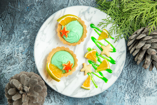 容器顶视图小馅饼与绿色糕点奶油和柠檬片板松枝在黑暗的桌子上晚餐树枝午餐