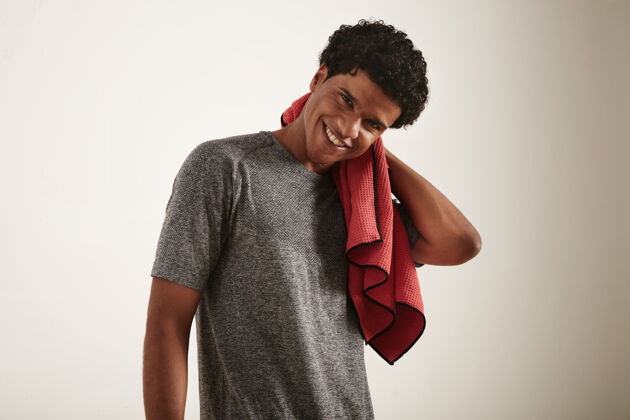 锻炼年轻的笑容可掬的深色卷发非裔美国运动员 穿着灰色技术t恤 用白色的华夫格超细纤维毛巾擦拭脖子自信模特成人