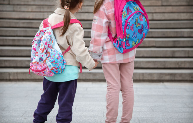 台阶两个背着漂亮背包的小女孩一起上学 手拉手 近距离接触童年友谊的概念姐妹小学生女孩