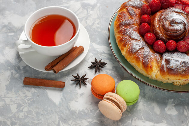 桌子在白色的桌子上 可以看到美味的草莓派 麦卡龙和一杯茶草莓饼干早餐