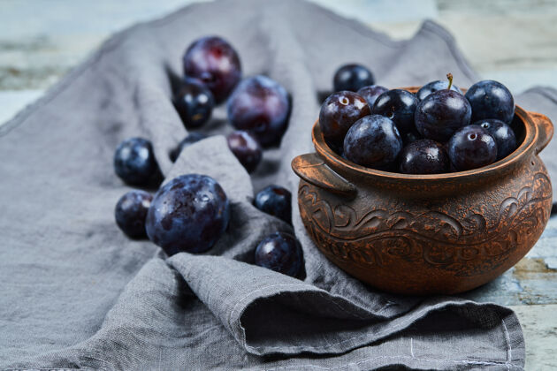 多汁在灰色桌布上的碗里种李子蓝色紫色水果