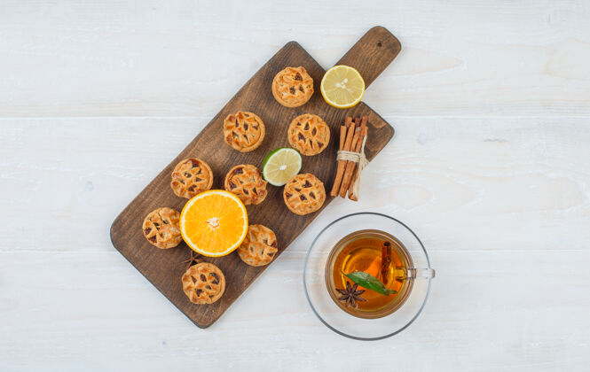 食物俯视图一个橘子 酸橙 饼干和肉桂在切菜板与一杯茶在白色的表面明星秋天饼干切刀