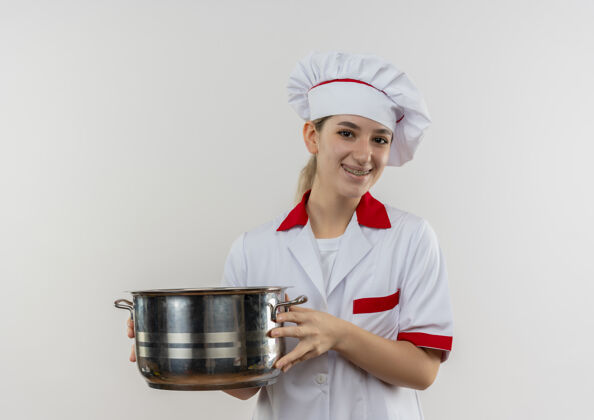 烹饪面带微笑的年轻漂亮厨师穿着厨师制服 戴着牙套 拿着一个看起来孤立的罐子站在白色的空间里牙科制服厨师