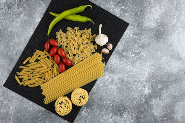 食品各种生面食和蔬菜放在黑竹板上干生的意大利面